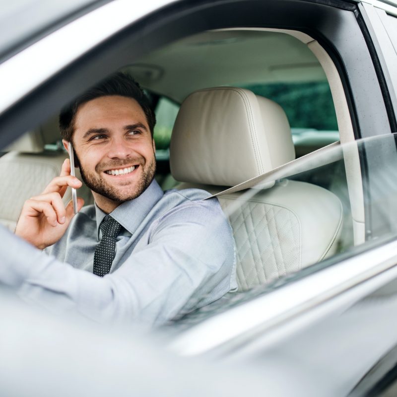 Young businessman with shirt, tie and smartphone sitting in car